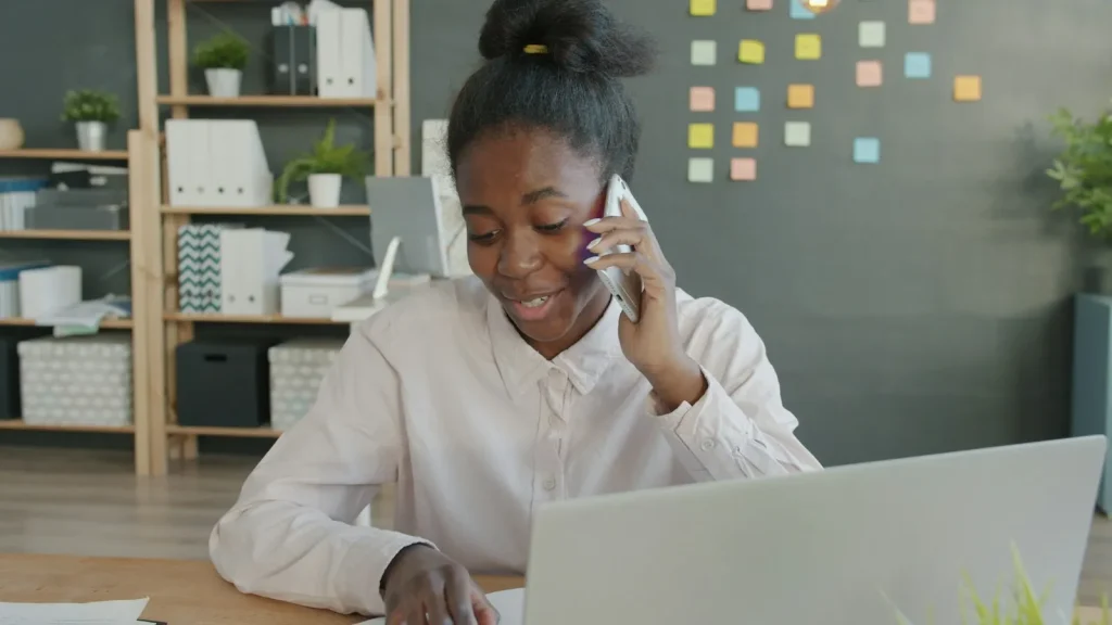 Smiling woman taking a customer phone call at an office desk with a laptop